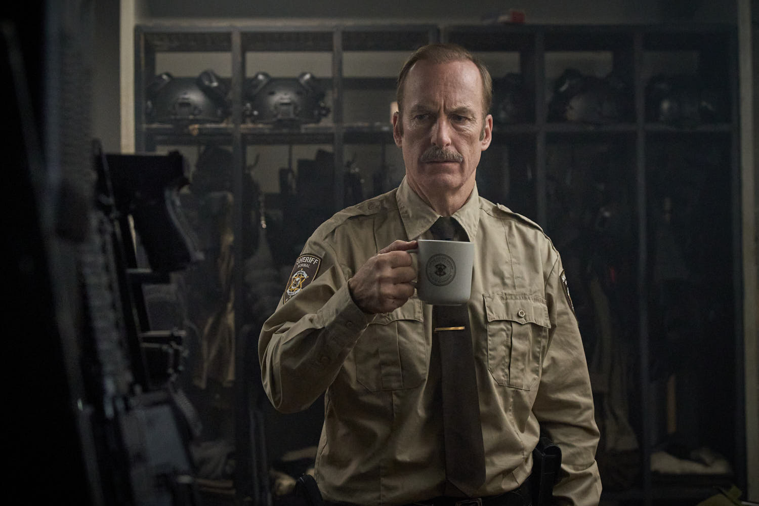 映画『NORMAL/ノーマル』武器庫でコーヒーを手にするボブ・オデンカーク演じるユリシーズ